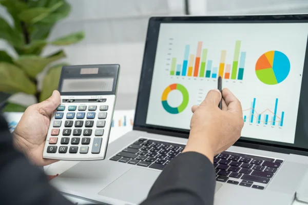 Someone holding a calculator and comparing the numbers to colorful chart such as bar chart, pie graph, and line chart.

Accounting software showing financial reports with bar charts and pie graph, Envato